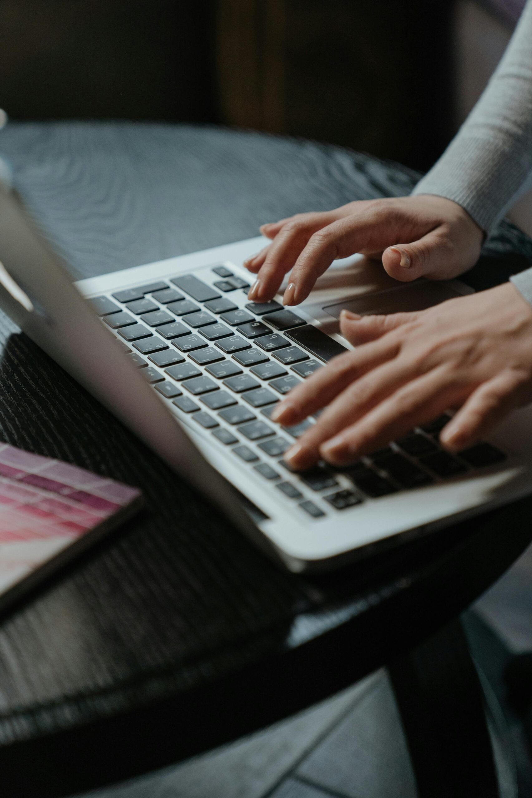 Close-up of woman's hands typing on a laptop keyboard indoors on a table.